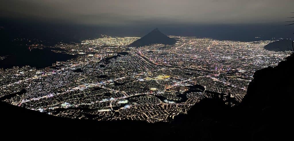 Night view of Monterrey city lights from El Teleférico on Cerro de la Silla, with mountain silhouettes in the distance